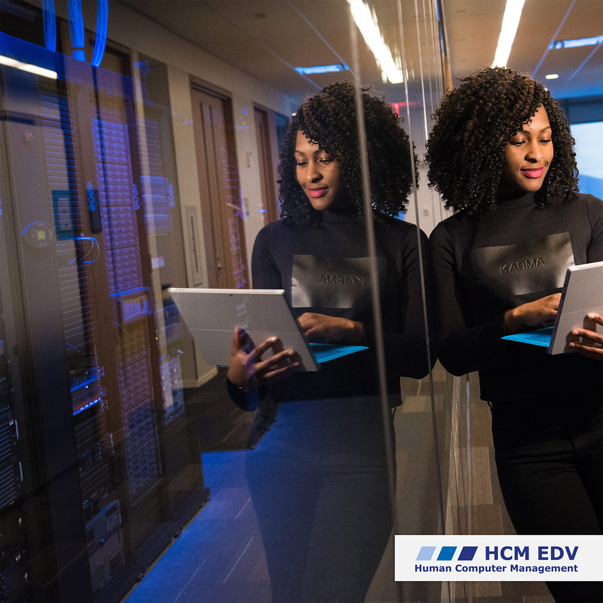 afroamerikanische Frau, die mit einem Laptop in der Hand vor einem Serverraum lehnt